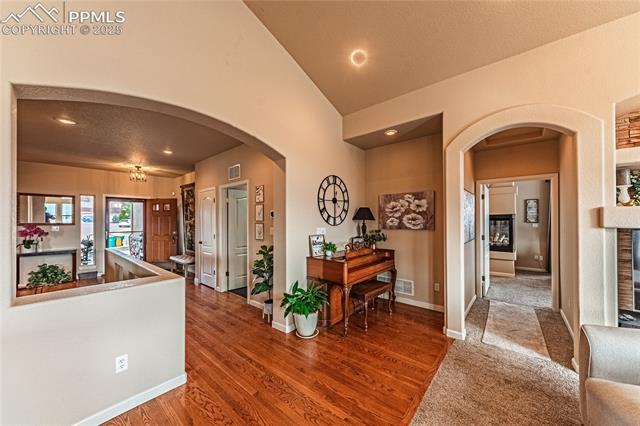 13812 Windy Oaks Road Colorado Springs, CO 80921 - Photo 19 of 50 Corridor with vaulted ceiling, wood finished floors, baseboards, visible vents, and arched walkways