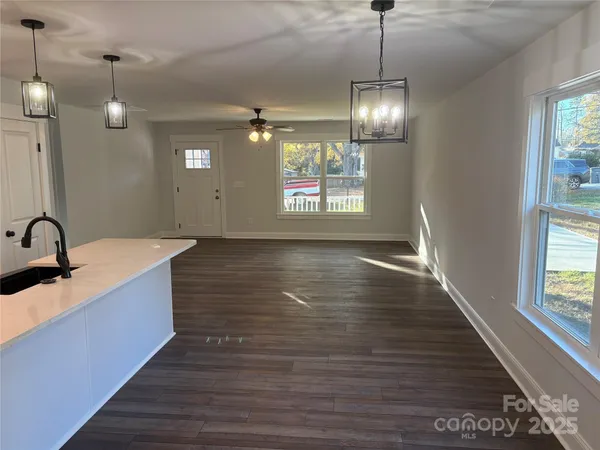 a view of a room with wooden floor chandeliers and kitchen view