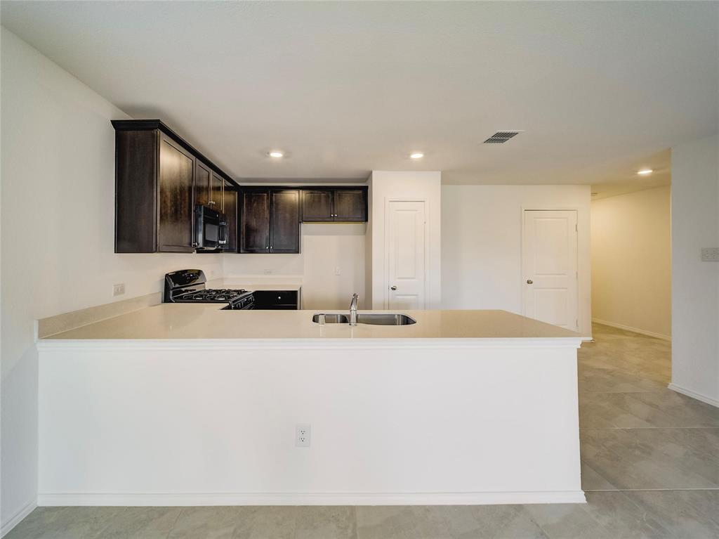357 Sun Bluff Road Fort Worth, TX 76052 - Photo 11 of 35 Kitchen featuring dark wood cabinetry, light-toned countertops, a black gas range, and a stainless steel sink