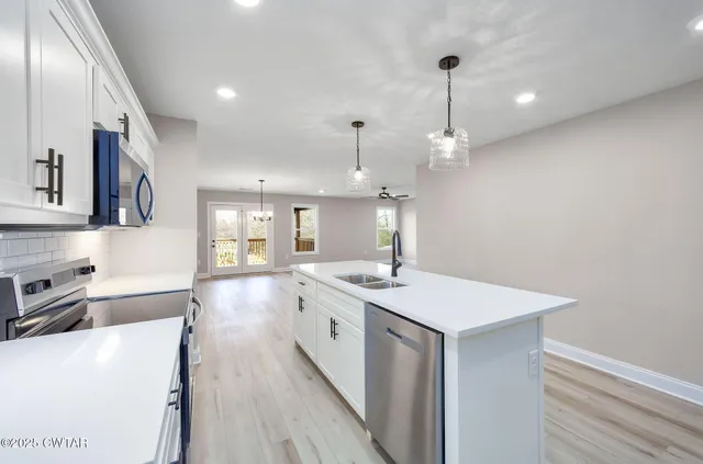 a large kitchen with stainless steel appliances a large counter top a sink a refrigerator and a window