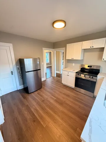 a kitchen with granite countertop a refrigerator a stove a sink dishwasher and white cabinets with wooden floor