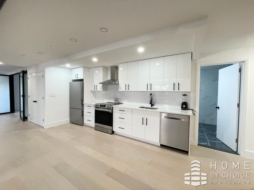 25 Peck Slip, Unit 3 Manhattan, NY 10038 - Photo 7 of 15 a large white kitchen with stainless steel appliances granite countertop a stove a sink a refrigerator and white cabinets with wooden floor