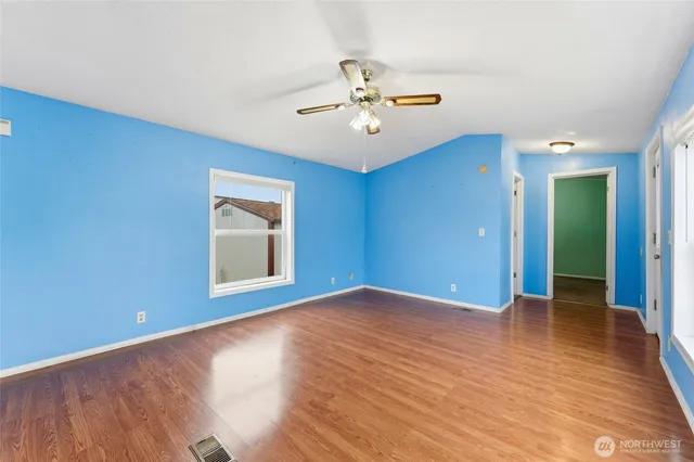 an empty room with wooden floor chandelier fan and windows