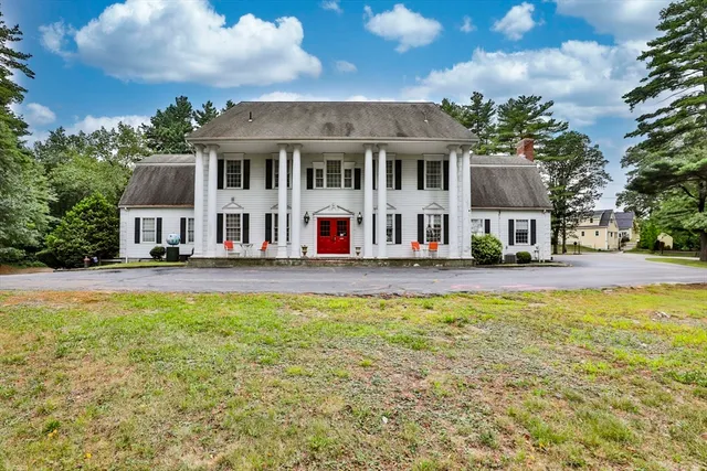a view of a white house with a large pool and lawn chairs under an umbrella