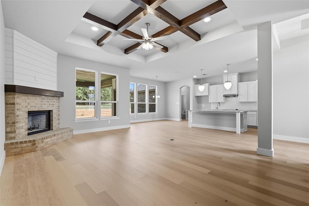 1005 Ronnie Court Springtown, TX 76082 - Photo 7 of 27 Unfurnished living room featuring coffered ceiling, arched walkways, a ceiling fan, a brick fireplace, and light wood finished floors