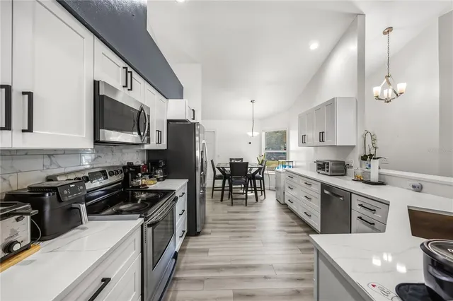 a kitchen with stainless steel appliances a stove top oven a sink a refrigerator white cabinets and wooden floor