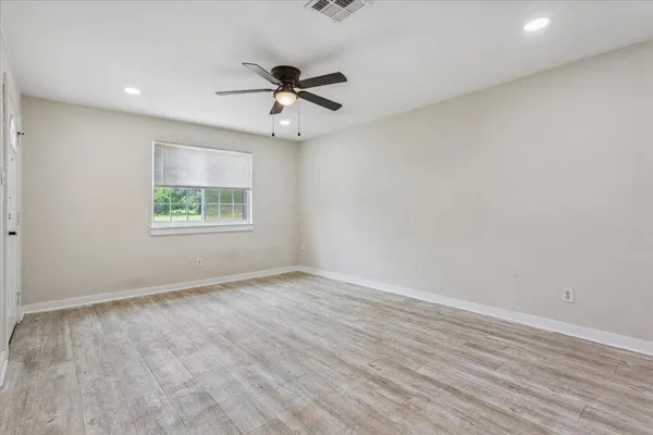 an empty room with wooden floor fan and windows