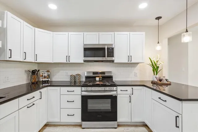 a kitchen with stainless steel appliances granite countertop white cabinets a stove a sink and a white