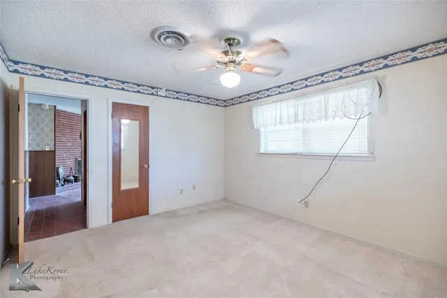a view of an empty room with a chandelier fan and a bathroom