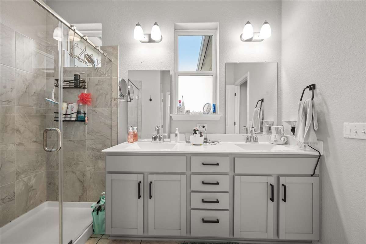 9015 Cattle Baron Path, Unit 1203 Austin, TX 78747 - Photo 16 of 23 Bathroom featuring double vanity, a textured wall, and a stall shower