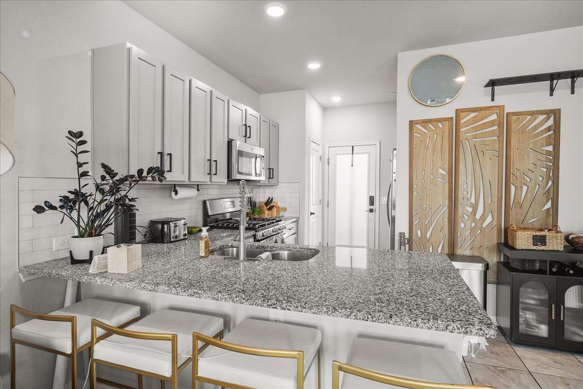 9015 Cattle Baron Path, Unit 1203 Austin, TX 78747 - Photo 3 of 23 Kitchen featuring a peninsula, light stone counters, stainless steel appliances, a kitchen breakfast bar, and gray cabinetry