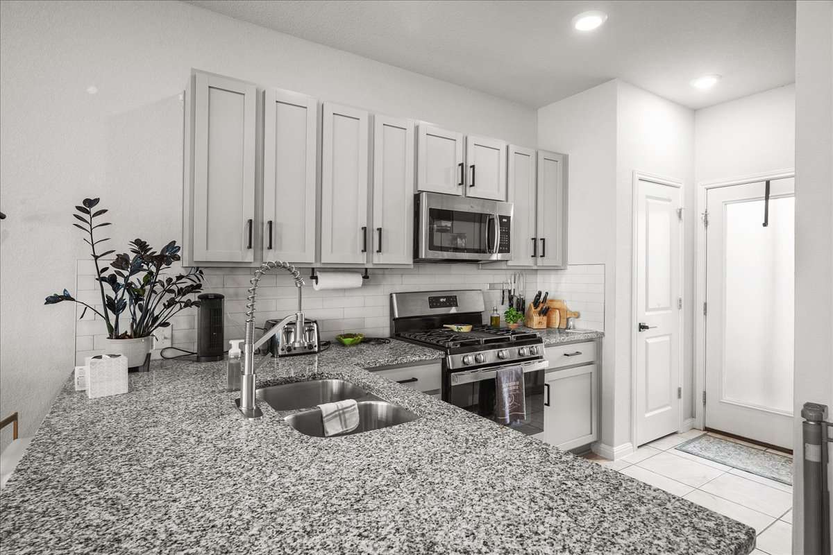 9015 Cattle Baron Path, Unit 1203 Austin, TX 78747 - Photo 4 of 23 Kitchen featuring light stone countertops, stainless steel appliances, tasteful backsplash, light tile patterned floors, and gray cabinets