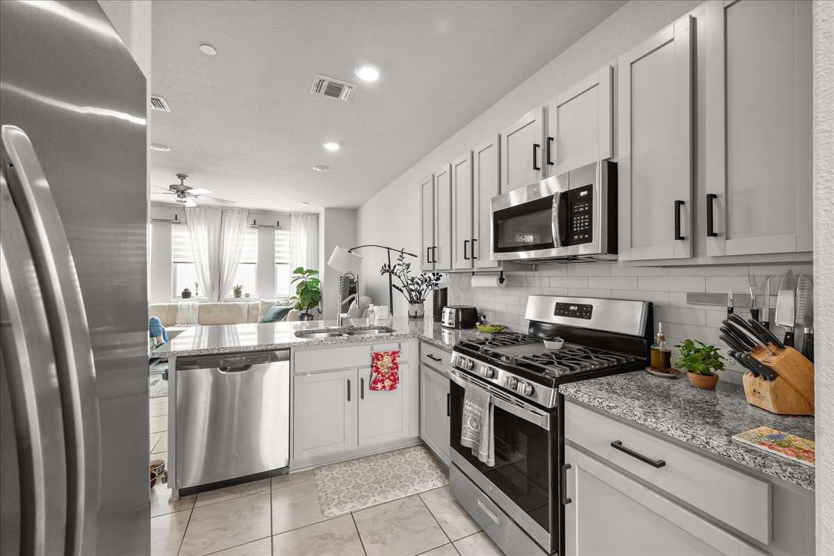 9015 Cattle Baron Path, Unit 1203 Austin, TX 78747 - Photo 23 of 23 Kitchen with stainless steel appliances, light stone countertops, a peninsula, ceiling fan, and open floor plan
