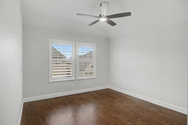 an empty room with wooden floor ceiling fan and windows