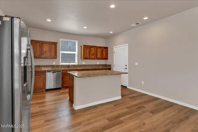 a kitchen with stainless steel appliances granite countertop a stove top oven a refrigerator a sink and dishwasher with wooden floor