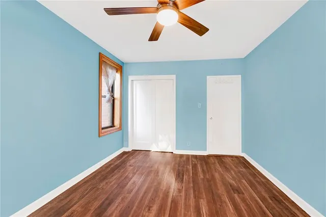 an empty room with wooden floor ceiling fan and windows