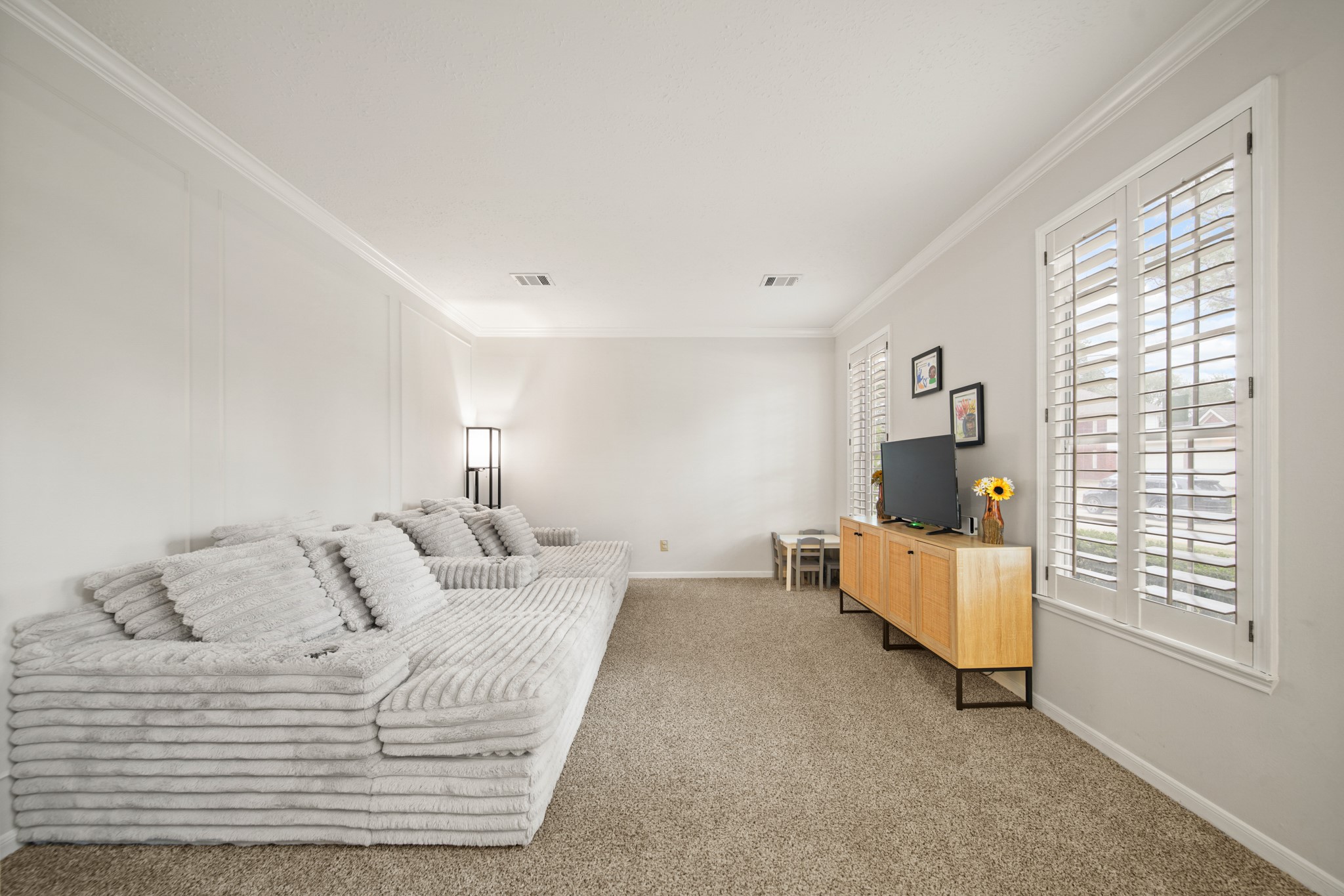 16114 Kintyre Point Road Houston, TX 77095 - Photo 13 of 44 Bright and cozy living room with neutral tones, featuring a plush sectional sofa, carpeted floor, and ample natural light from shuttered windows.