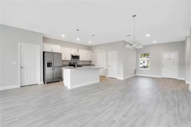 a view of an empty room and kitchen with hardwood floor