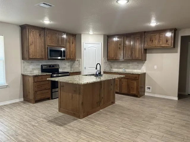 a kitchen with stainless steel appliances granite countertop a sink a stove a refrigerator cabinets and a wooden floor