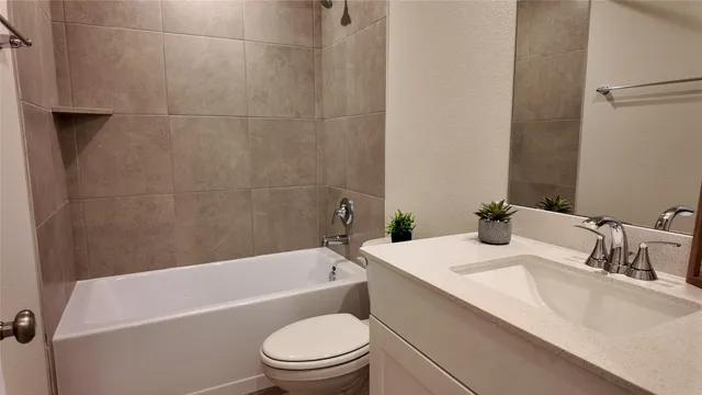 a bathroom with a granite countertop bathtub shower sink vanity mirror and toilet