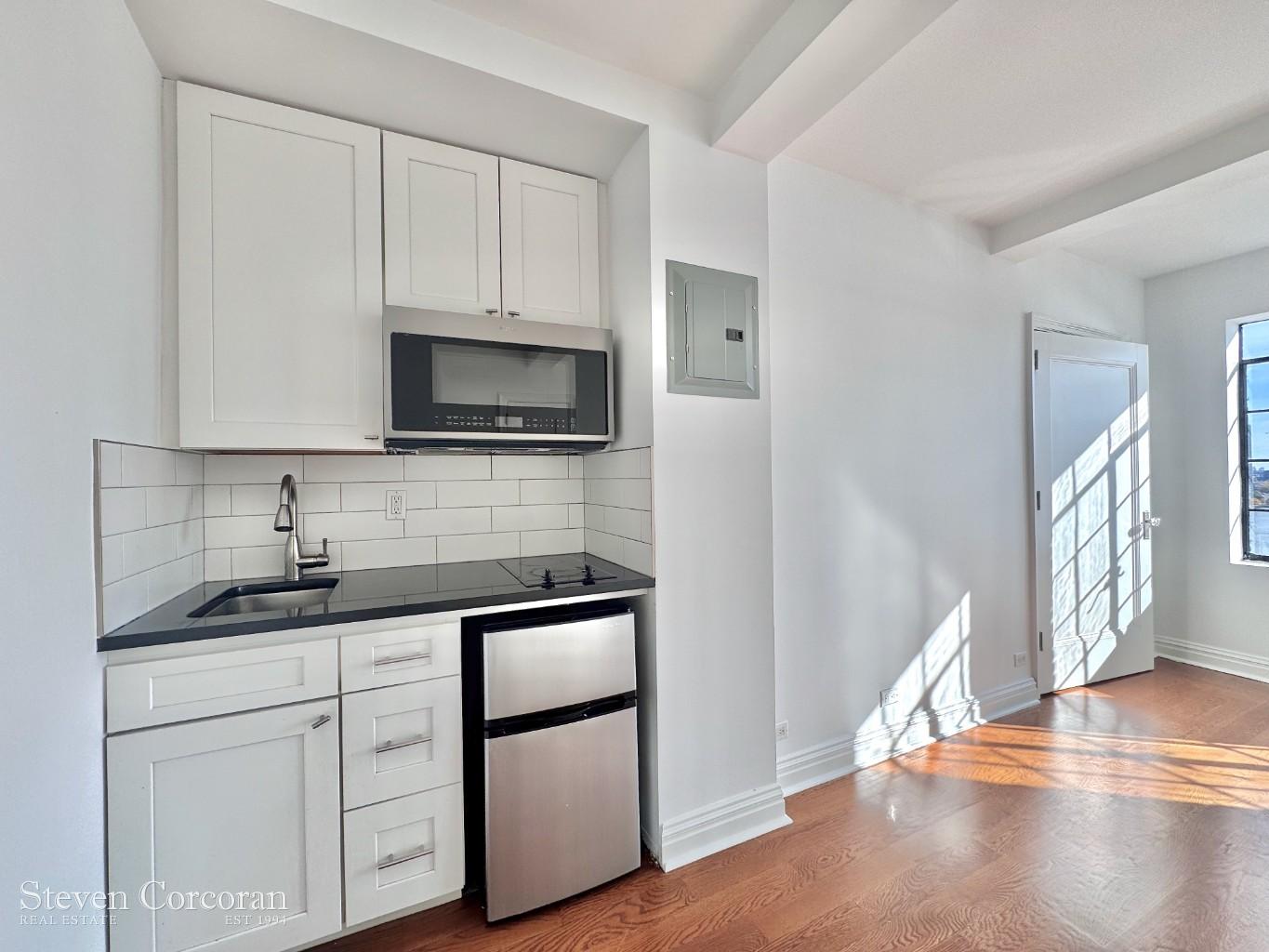5 Tudor City Place, Unit 1026 Manhattan, NY 10017 - Photo 5 of 8 a kitchen with granite countertop white cabinets and white appliances
