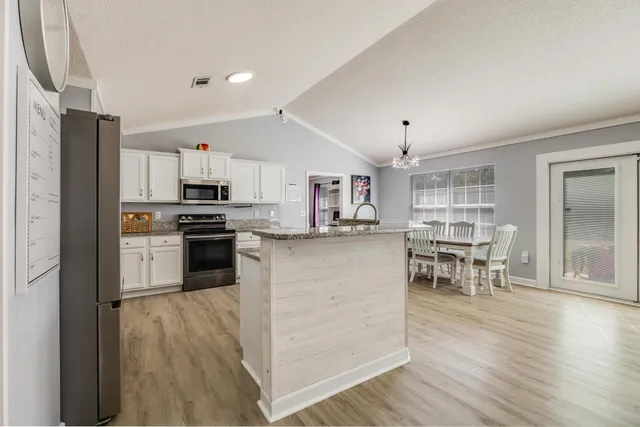 a kitchen with stainless steel appliances kitchen island granite countertop a stove top oven a sink a dining table and chairs with wooden floor