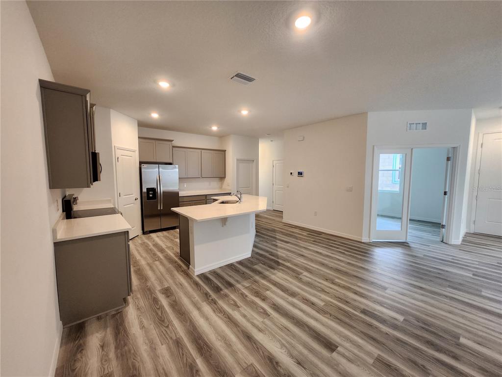 32760 Rustic Rise Road San Antonio, FL 33576 - Photo 6 of 27 a large open kitchen with stainless steel appliances kitchen island a stove a refrigerator a sink dishwasher with a dining table and chairs with wooden floor