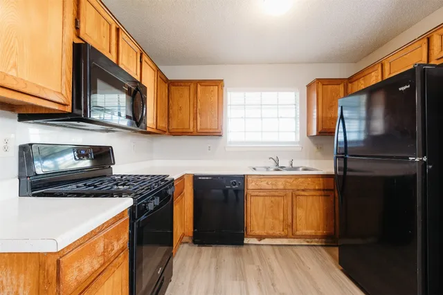 a kitchen with stainless steel appliances granite countertop a refrigerator a sink dishwasher a stove and white countertops with wooden floor