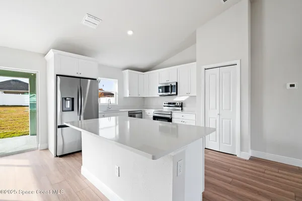 a kitchen with stainless steel appliances a microwave a stove a sink a refrigerator and white cabinets with wooden floor