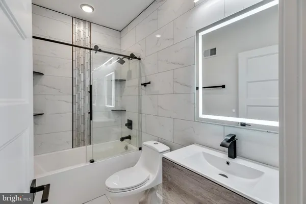 a bathroom with a bathtub shower sink vanity mirror and toilet