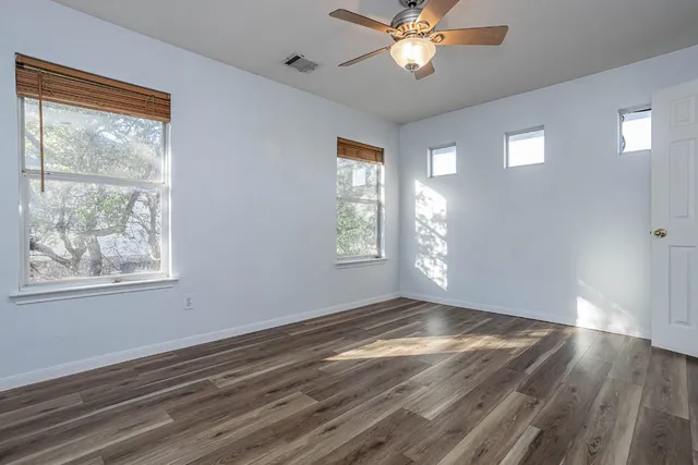 an empty room with wooden floor chandelier fan and windows