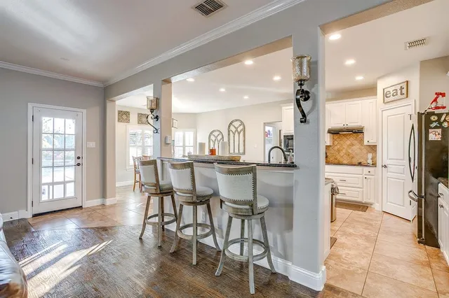 a room with stainless steel appliances kitchen island granite countertop a refrigerator a stove a dining table and chairs with wooden floor