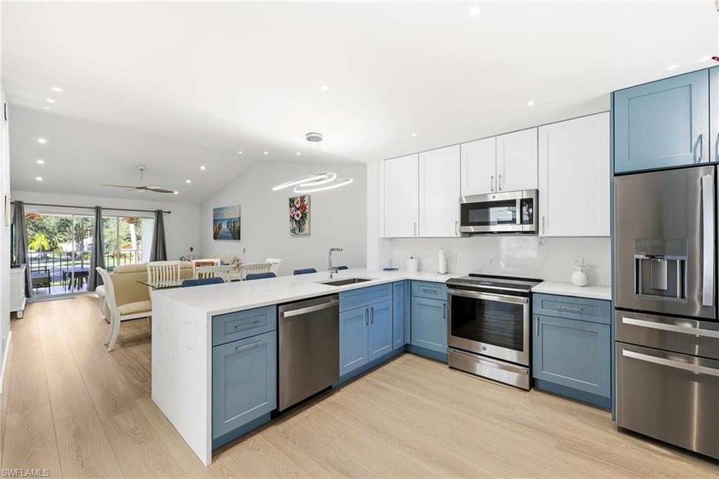 7707 Jewel Lane, Unit 201 Naples, FL 34109 - Photo 8 of 31 Kitchen featuring appliances with stainless steel finishes, blue cabinets, white cabinetry, a peninsula, and light wood-style flooring