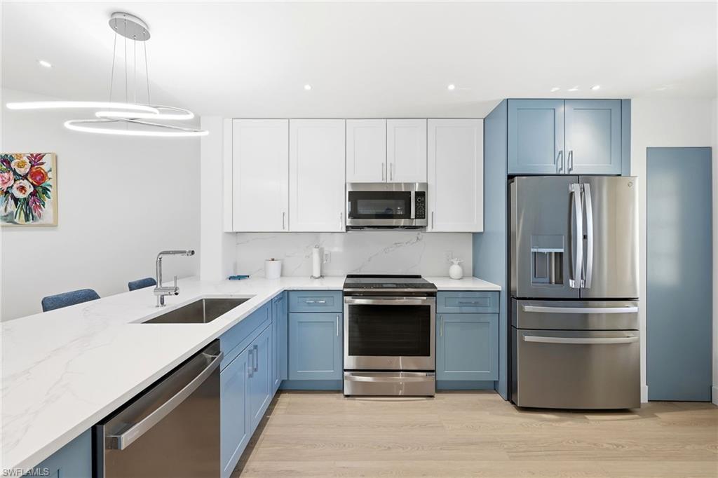 7707 Jewel Lane, Unit 201 Naples, FL 34109 - Photo 9 of 31 Kitchen featuring blue cabinetry, appliances with stainless steel finishes, white cabinetry, light wood finished floors, and light stone countertops