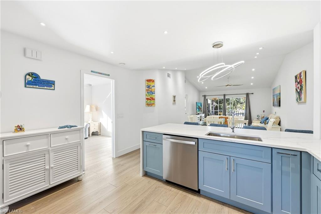 7707 Jewel Lane, Unit 201 Naples, FL 34109 - Photo 31 of 31 Kitchen featuring blue cabinetry, lofted ceiling, stainless steel dishwasher, light stone countertops, and open floor plan