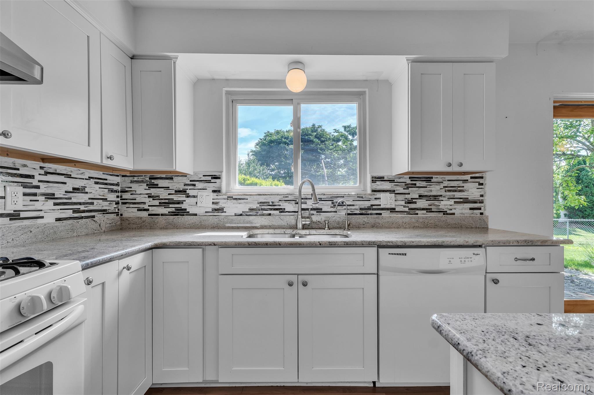 7000 Woonsocket Street Canton, MI 48187 - Photo 21 of 65 Modern kitchen featuring white cabinetry with silver hardware, speckled countertops, a mosaic tile backsplash, a stainless steel sink with a gooseneck faucet, and a window above the sink