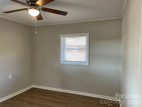 an empty room with wooden floor chandelier fan and windows