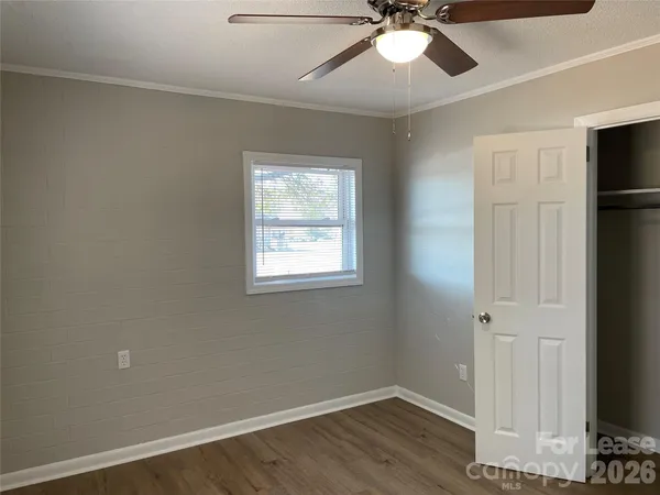 a view of an empty room with wooden floor and a ceiling fan