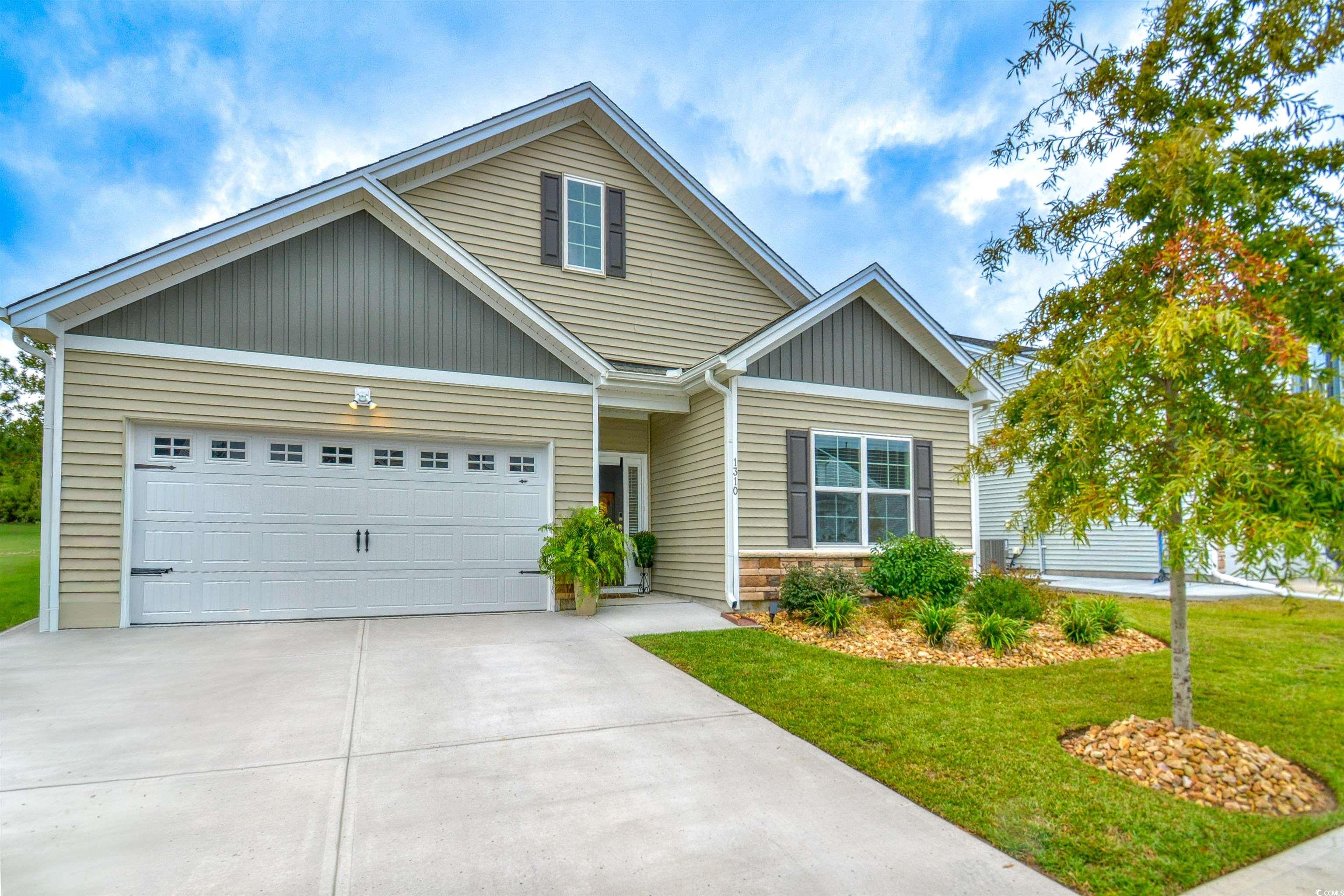 View of front of property featuring a front yard, driveway, stone siding, an attached garage, and board and batten siding