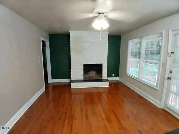 a view of an empty room with wooden floor fireplace and a window