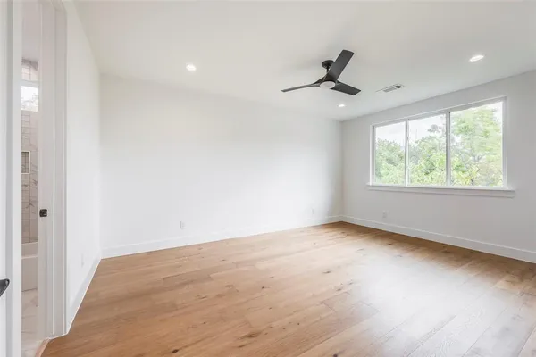 an empty room with wooden floor ceiling fan and windows