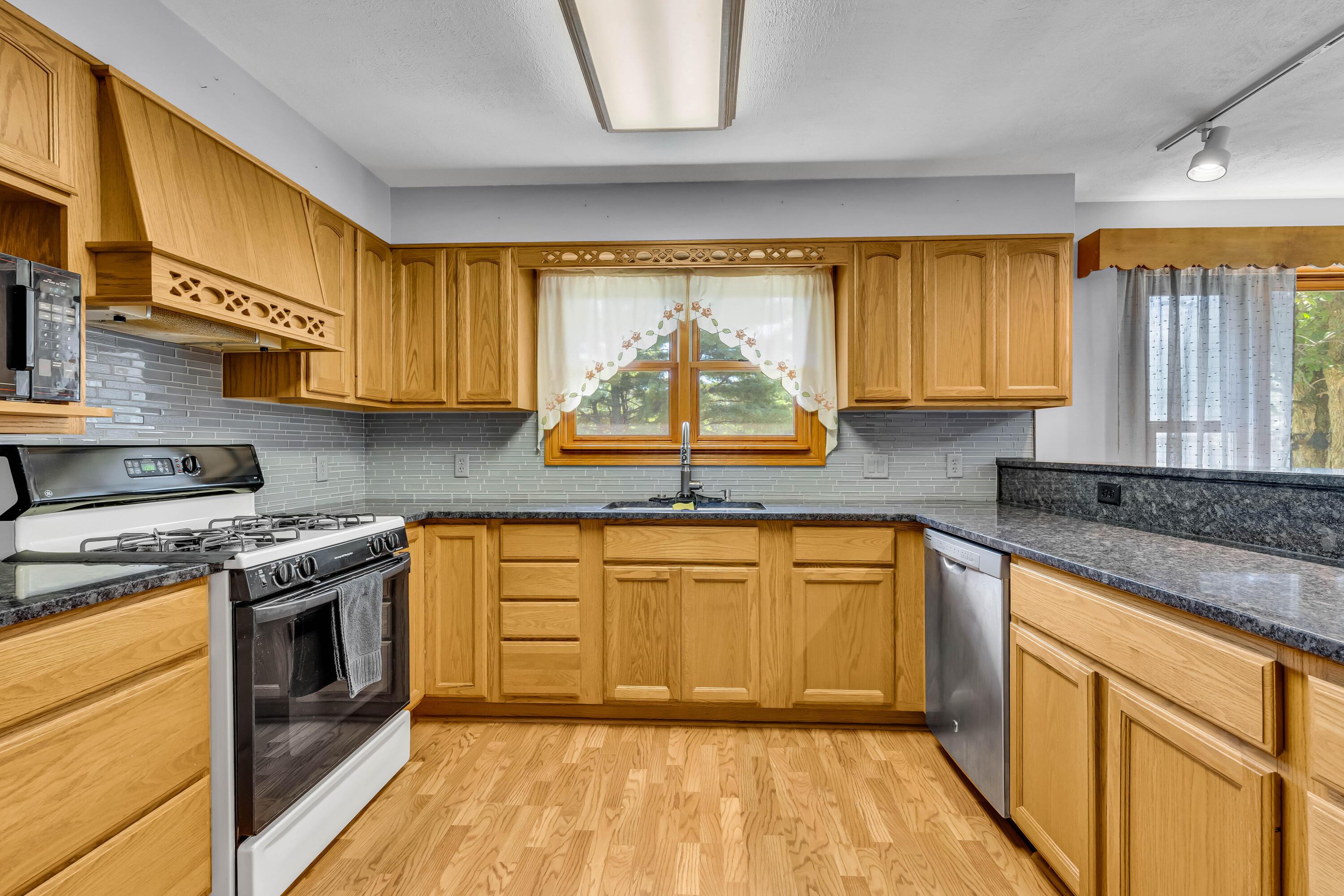 1213 East Cooke Road Columbus, OH 43224 - Photo 21 of 57 • Laminate flooring • Tan painted walls • Oak cabinets • New granite countertops ~ 2020 • Breakfast bar ledge • Track lighting • Kenmore® refrigerator • Tappan® microwave • General Electric® gas stove • New General Electric dishwasher ~ 2020 • Insinkerator® disposal • Glass tile backsplash • Single bowl, stainless steel sink with soap dispenser • Ceiling light • Pantry closet