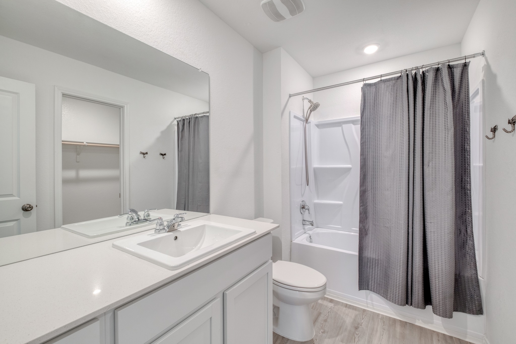 23412 Tiny Moons Way Elgin, TX 78621 - Photo 25 of 38 Contemporary bathroom featuring a white vanity with integrated sink, a large wall-mounted mirror, white bathtub with a shower kit, and light wood-finish flooring