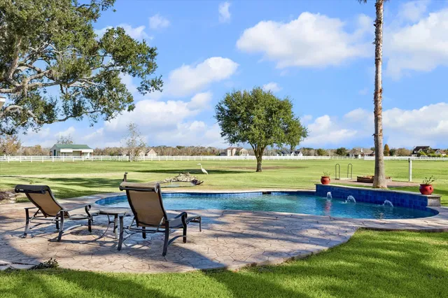 a view of a swimming pool with lawn chairs and a big yard