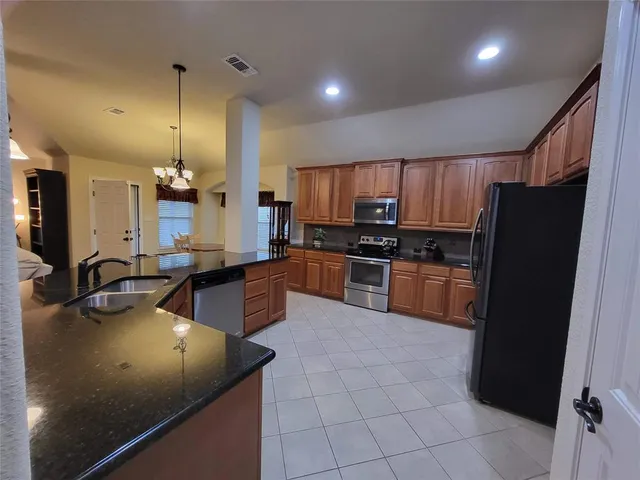 a kitchen with granite countertop a refrigerator a sink a stove top oven and cabinets