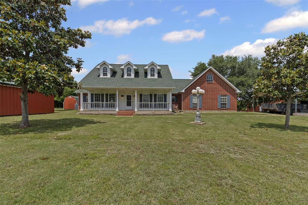 Cape cod home with a porch, a front lawn, roof with shingles, brick siding, and an outbuilding