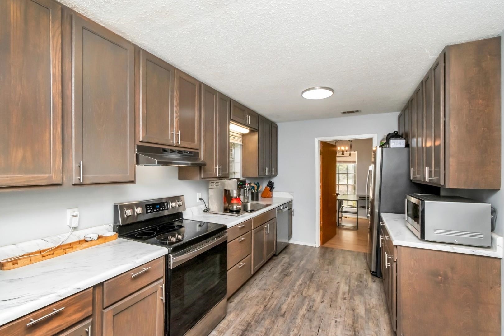6405 1st Street Wilmer, AL 36587 - Photo 7 of 38 Kitchen with stainless steel appliances, a textured ceiling, light wood-type flooring, under cabinet range hood, and a chandelier