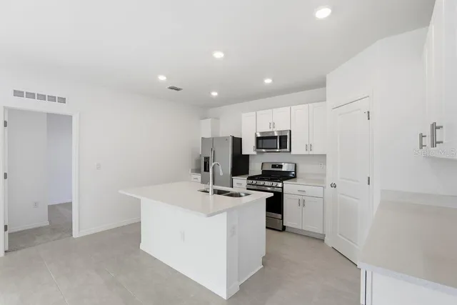 a kitchen with stainless steel appliances a stove top oven a refrigerator a sink and white cabinets