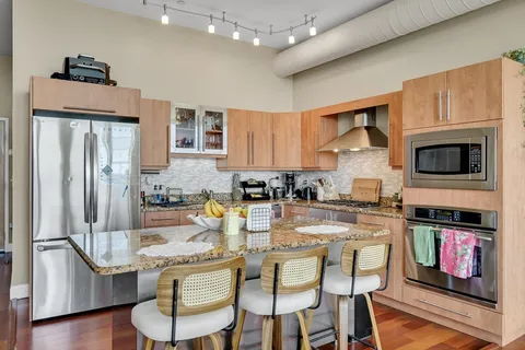 a kitchen with stainless steel appliances granite countertop a stove top oven a refrigerator a sink and dining table with wooden floor