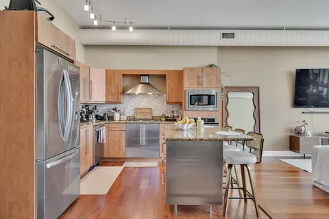 a kitchen with stainless steel appliances a refrigerator a stove a sink a dining table and chairs with wooden floor